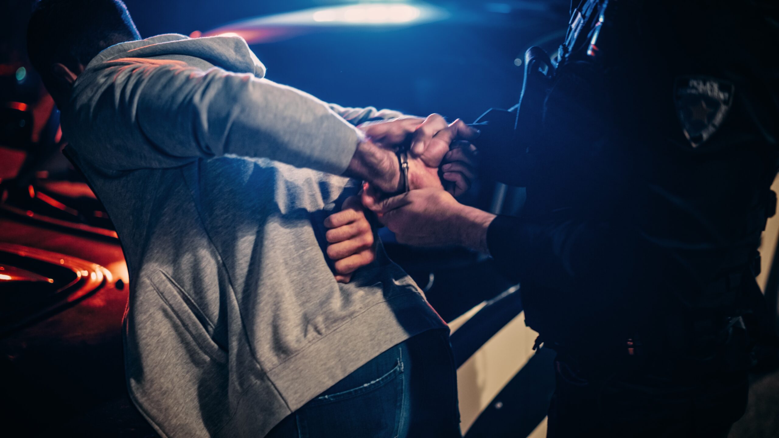 A person in a hoodie is handcuffed by an officer